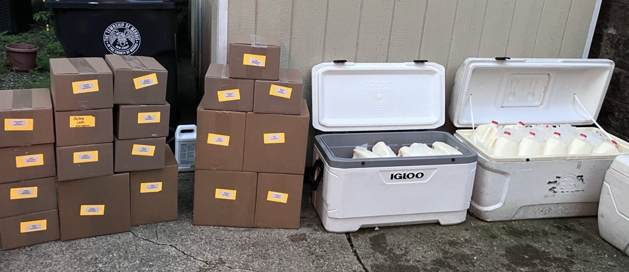 Boxed orders labelled with names, and coolers of milk jugs, waiting at a pickup spot